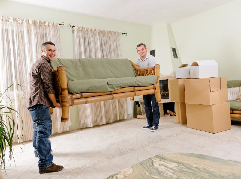 Furniture Removal Services Kent WA | Safe & Reliable Furniture Moving Two movers carrying a large sofa inside a home during a relocation project, showcasing professional Furniture Removal Services Kent WA with packed moving boxes in the background.